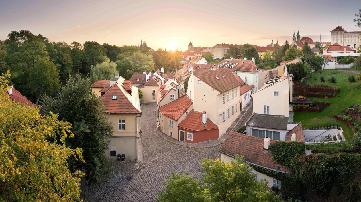 Cobblestone street lined with quaint houses and greenery at sunset.