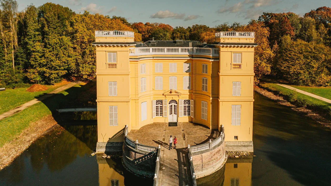 Yellow castle surrounded by a moat and autumn trees under a blue sky.