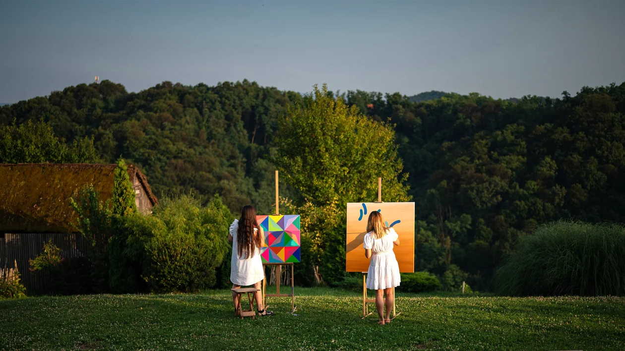 Two women painting on canvases in a grassy countryside setting