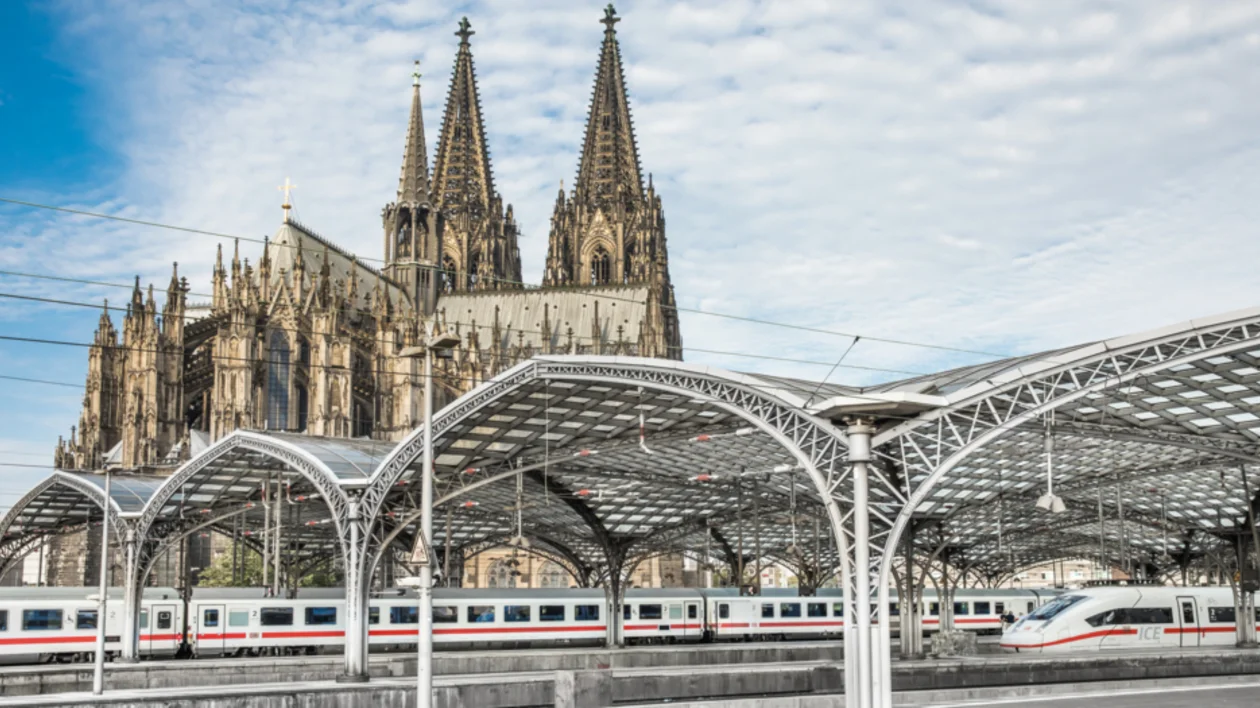 Train station with a modern canopy in front of a large Gothic cathedral.