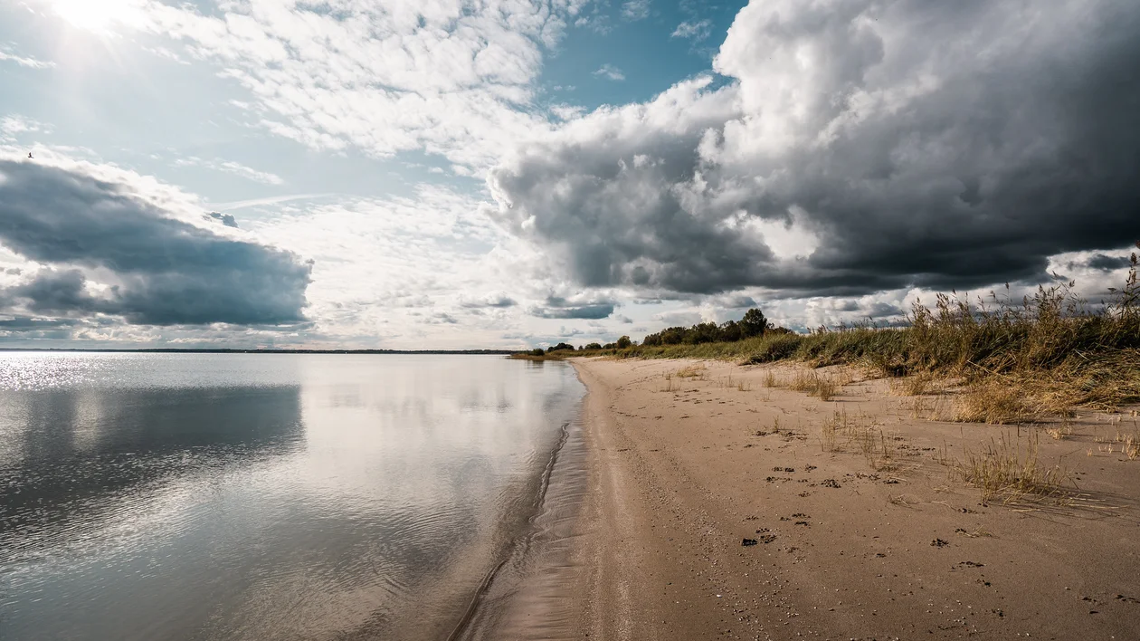 Sandy beach with calm water and dramatic clouds in the sky.