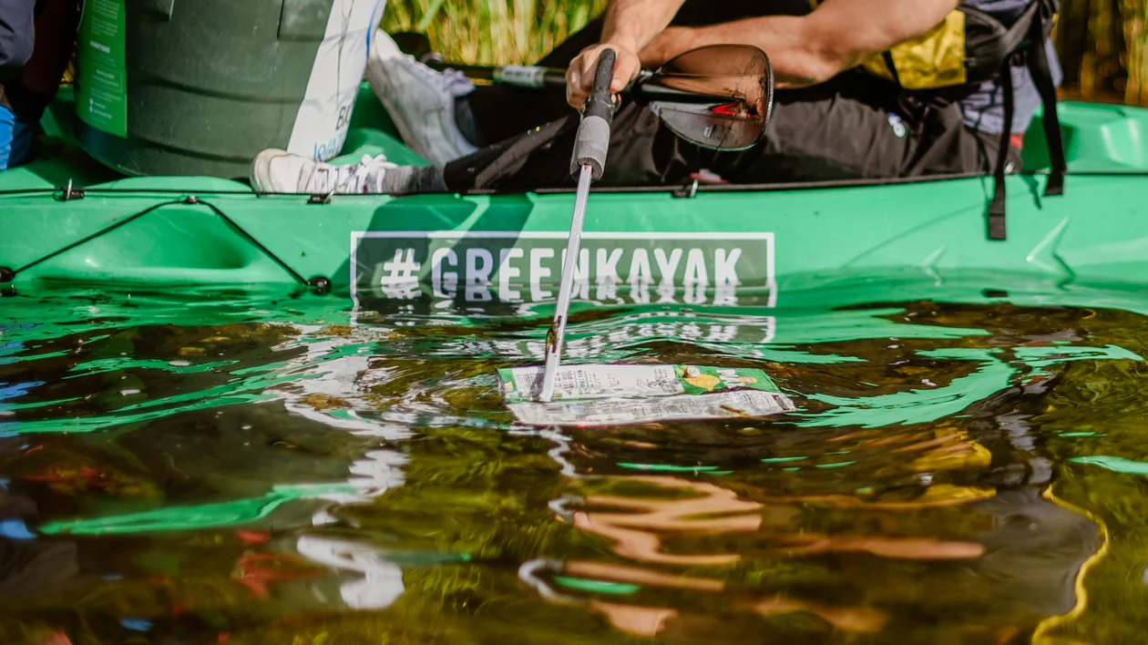 Person in a green kayak using a net to collect trash from the water.
