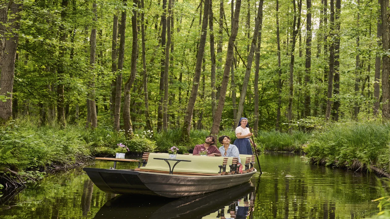 People on a small boat floating through a lush green forest.
