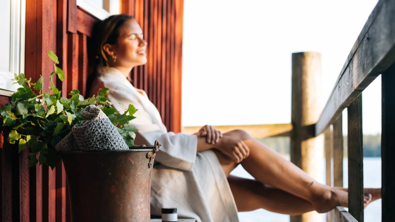Woman relaxing on a wooden porch by the water, sunlight on her face.