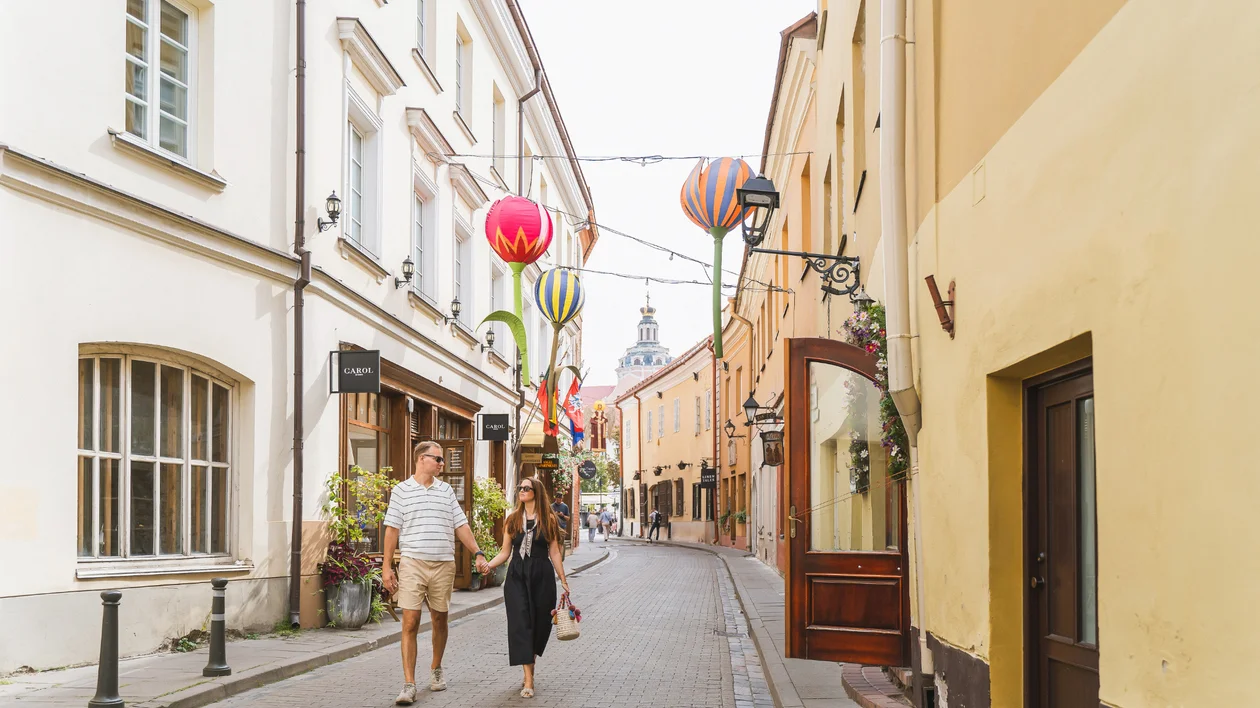 Couple walking on a narrow street decorated with colorful balloon sculptures.