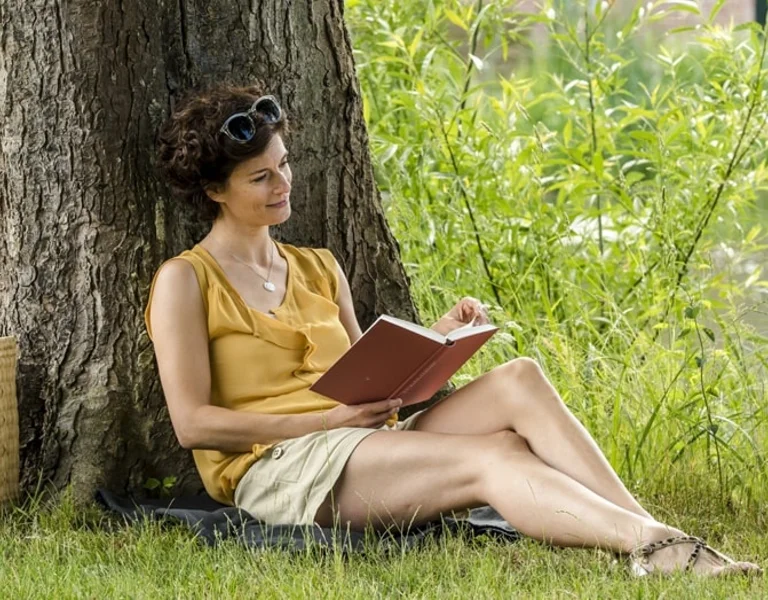 Woman reading a book leaning against tree, Germany