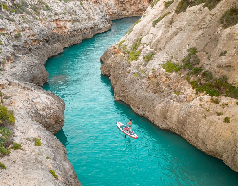 Person kayaking on turquoise water between rocky canyon walls.