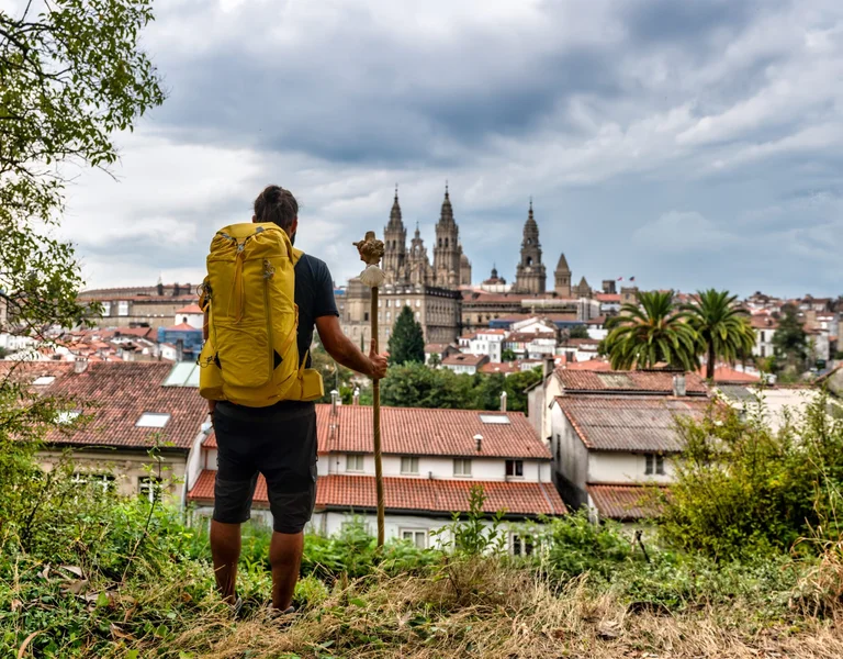 Pilgrims walking along the historic Camino de Santiago trail, surrounded by picturesque landscapes and ancient stone structures, as they make their way towards the shrine of Saint James in Santiago de Compostela, Spain.