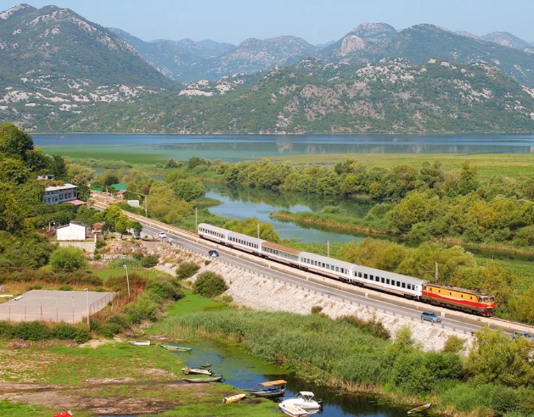 A train is passing through a stunning landscape between a lake and hills