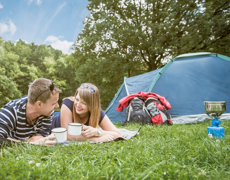 A couple is camping in the nature, with a tent and nature behind.