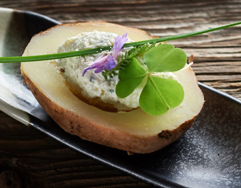 Find out how sophisticated a boiled potato can be, artfully topped with a dollop of soft cheese and garnished elegantly with a fresh herb sprig and a delicate edible flower.