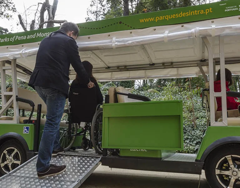 A person assists a wheelchair user onto an accessible electric park shuttle.