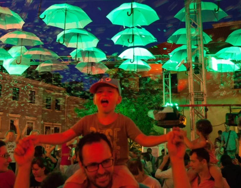Colorful umbrellas suspended above a crowd at a night event.