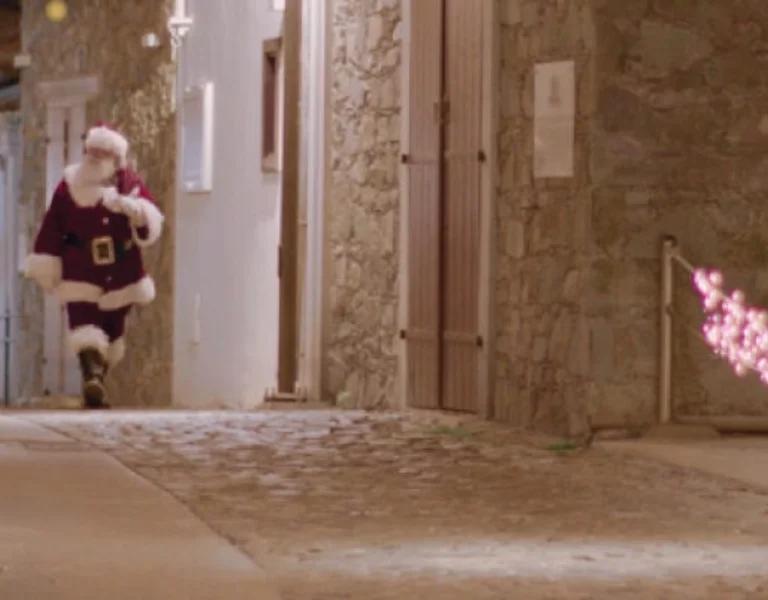 Santa Claus running down a cobblestone street with holiday lights.