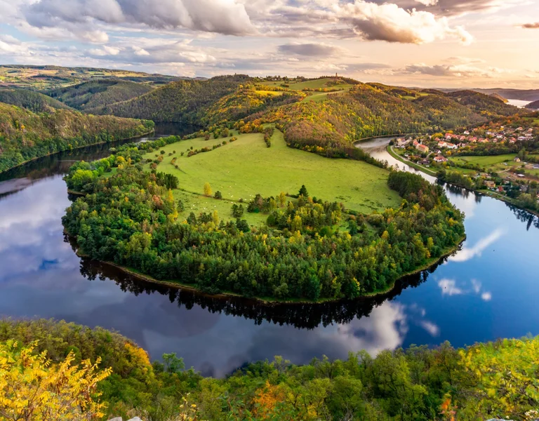 Aerial view of a meandering river through colorful autumn forests and a small village.