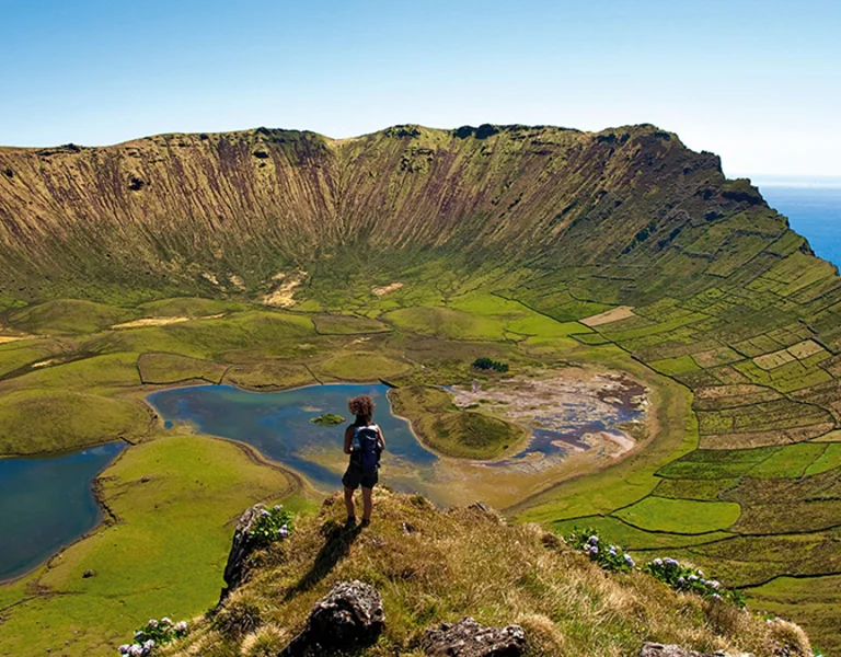 A hiker overlooking a green volcanic crater with lakes by the sea.