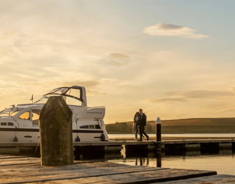 Sunset at a tranquil marina with a couple walking by a moored yacht.