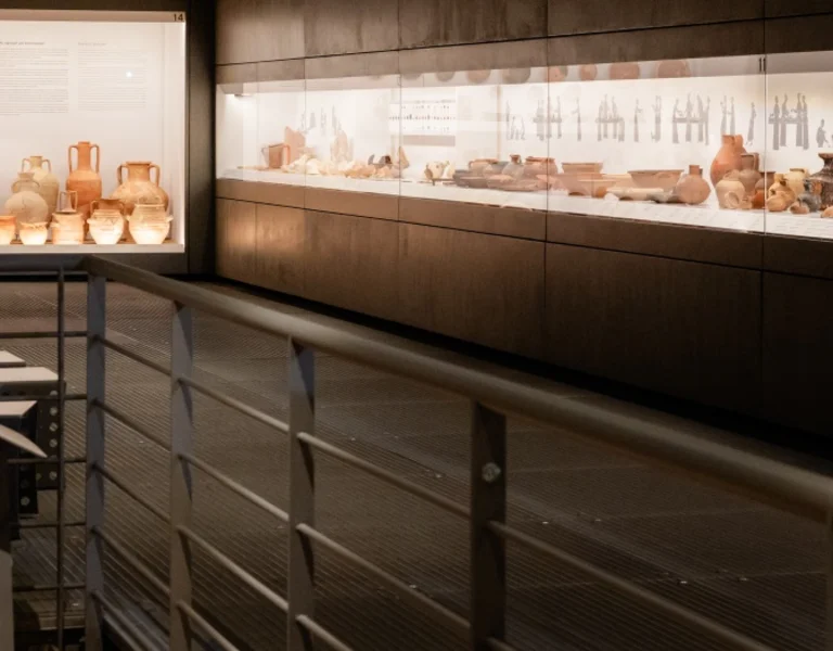 Interior of the Acropolis Museum in Greece displaying ancient pottery and artifacts in lit cases with explanatory texts.
