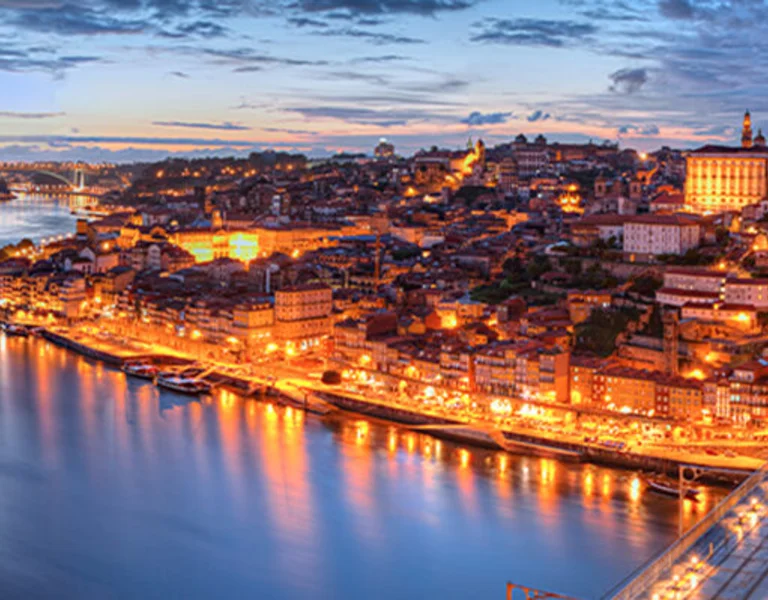 Twilight cityscape with a lit bridge over a river, reflecting lights on water.