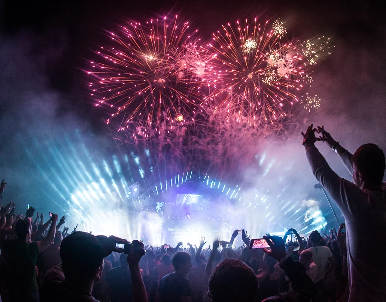 Crowd enjoying a fireworks display at a night concert with bright stage lights.