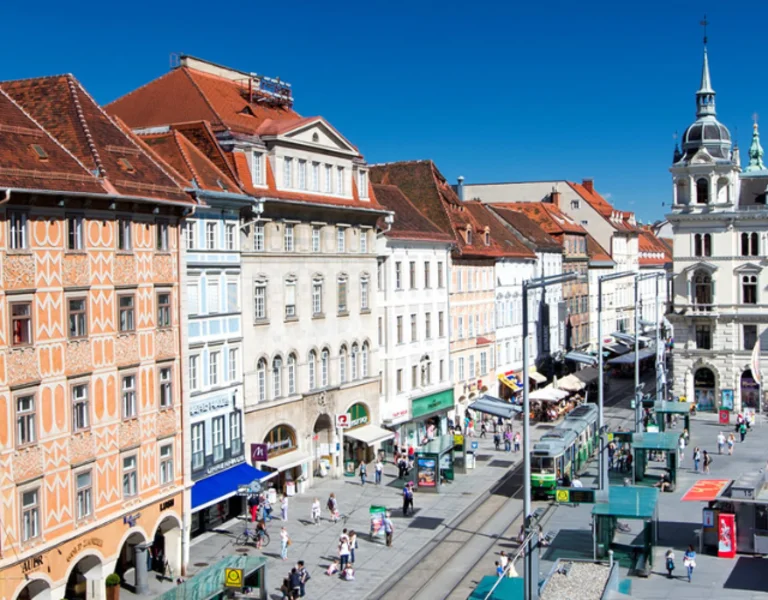 Sunny Graz square with ornate buildings, bustling market stalls, and pedestrians.