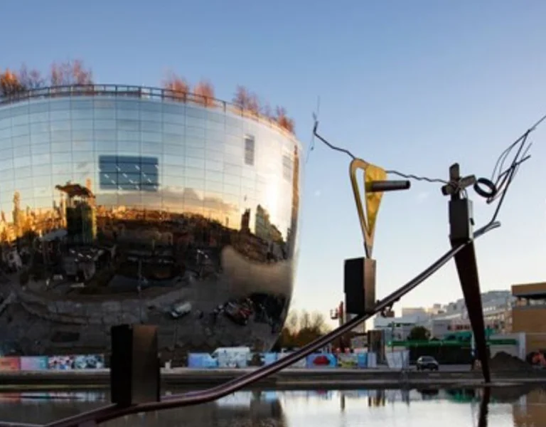 Depot Boijmans Van Beuningen, a modern cylindrical building with reflective facade by a pond with a sculpture in the foreground at dusk in Rotterdam.