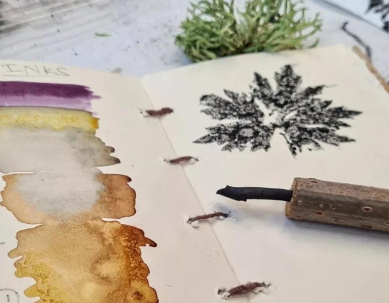 An open sketchbook features ink samples in various colors, notes on natural materials, and a handmade ink applicator.