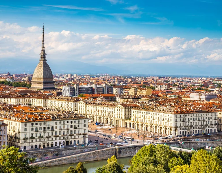 A panoramic view of Turin featuring the iconic Mole Antonelliana, overlooking historic buildings and the Po River beneath a blue sky.