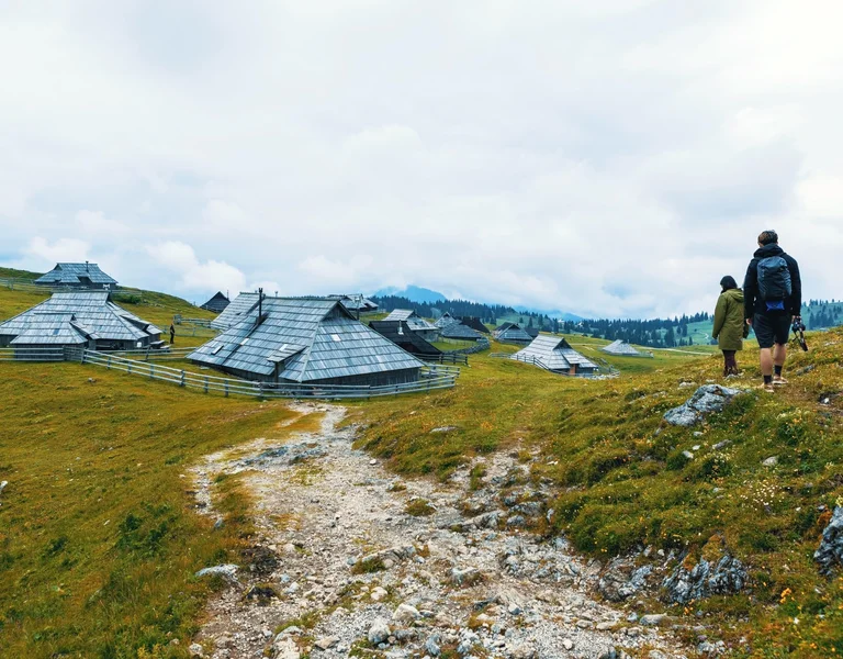 Traditional wooden shepherd huts scattered across the lush green pastures of Velika Planina, framed by rolling hills and dense forest.