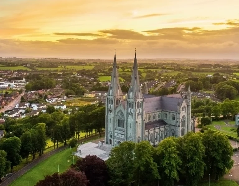 Aerial view of St. Patrick's Cathedral at sunset, surrounded by lush greenery and a small town in the foreground.