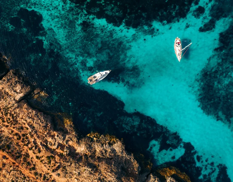 Aerial view of boats floating on the vibrant turquoise waters of the Blue Lagoon, Comino, Malta.