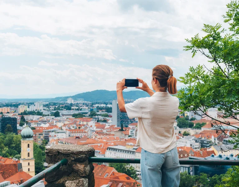 Woman tourist taking a picture of the city of Graz in Austria with panoramic view.