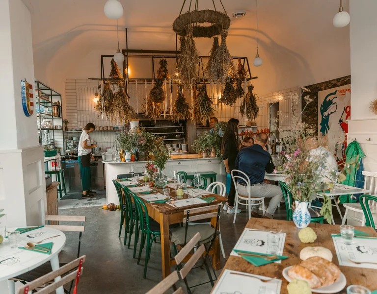 Interior of Wild Kitchen Modra in Slovakia, with hanging herbs, rustic décor, and guests dining in a cosy atmosphere