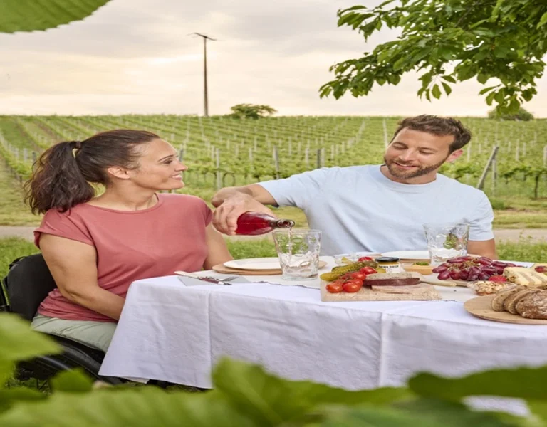 Couple enjoying a picnic with wine, bread, cheese and fresh produce in a vineyard in Germany during summer.