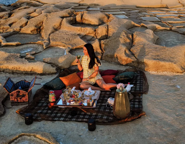 Woman having a sunset picnic on the rocky coast of Malta, with traditional food, wine, and sea views.