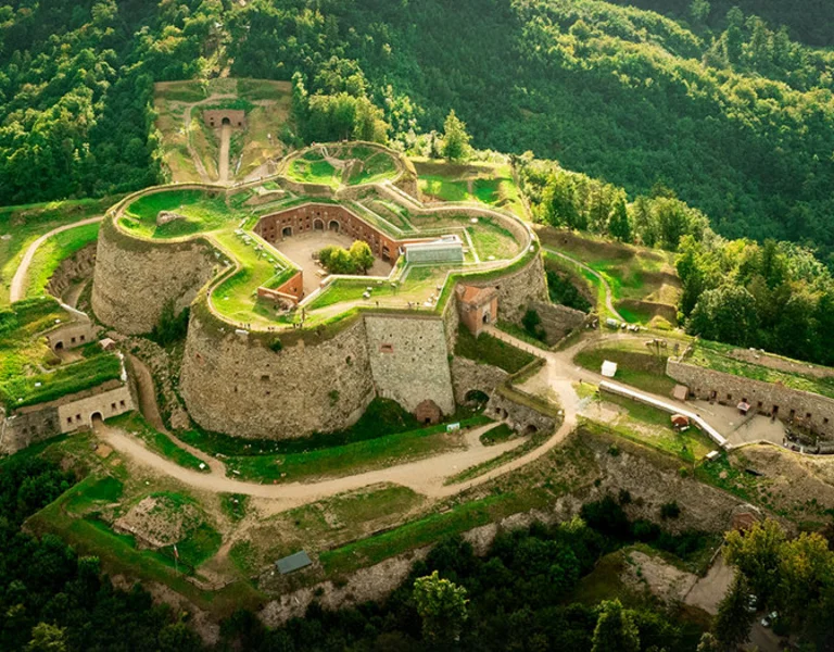 Bird’s-eye view of Srebrna Gora Fortress surrounded by lush greenery, bathed in warm sunlight highlighting its historic stone walls.