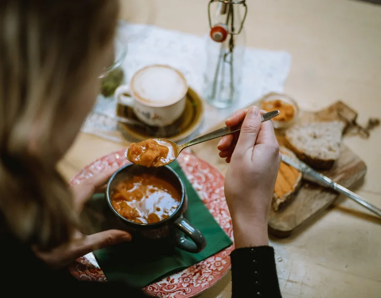 Close-up of a woman enjoying a warm bowl of soup at a cozy café table, with bread, spread, and a cup of coffee beside her in Doetinchem, the Netherlands.