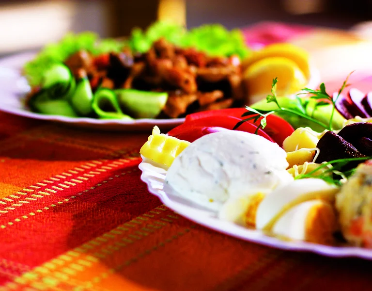 Traditional Bulgarian appetizers with cheese, eggs, fresh vegetables, and herbs served on a festive table with a red woven tablecloth.