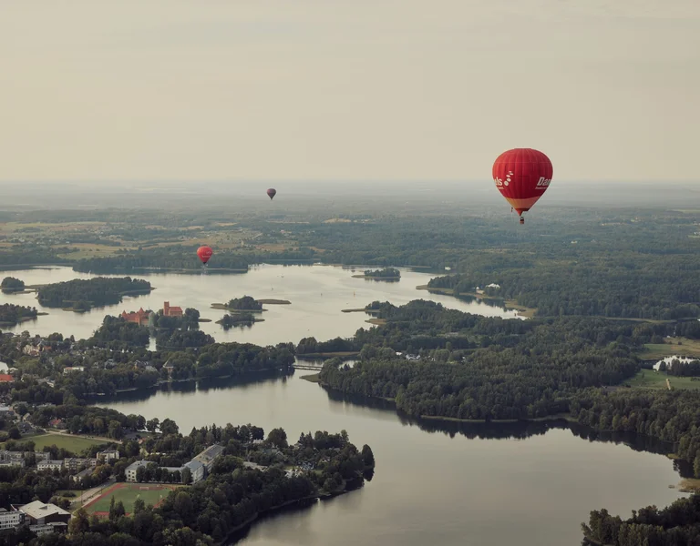 Hot air balloons floating above lakes and islands near Trakai, Lithuania, offering scenic aerial views at sunset.
