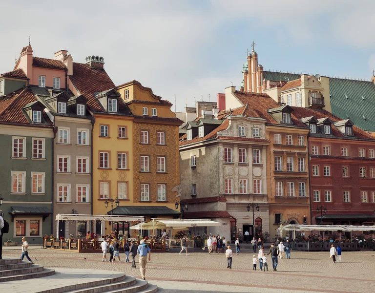 Colorful historic townhouses in Warsaw’s Old Town Market Square with people strolling and dining outdoors.