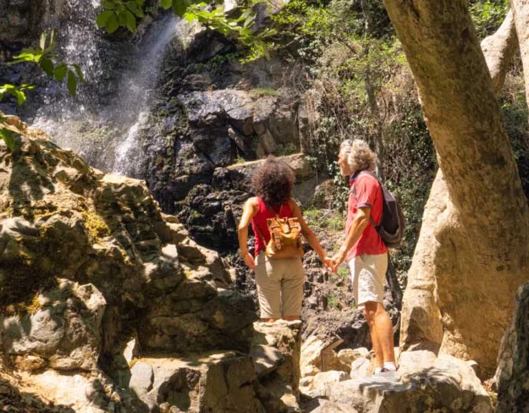 Two hikers walking toward a waterfall in a rocky forest