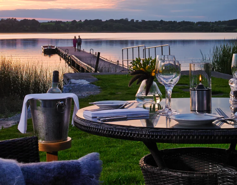 Romantic lakeside dinner table set at sunset beside a quiet pier