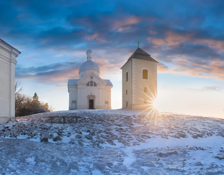 Snow-covered hilltop chapel and bell tower at sunrise in Mikulov