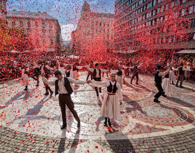 Dancers in traditional costumes perform outdoors as red confetti falls around them.