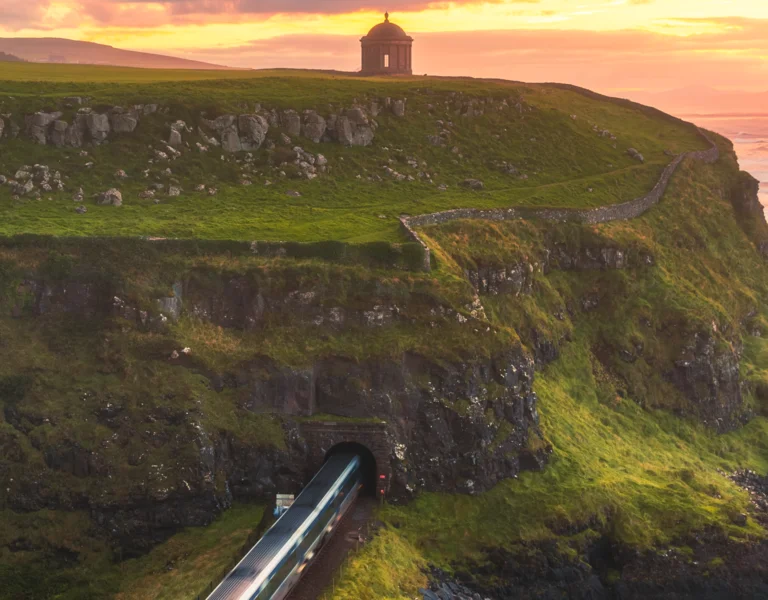 Green cliffs overlooking the ocean at sunset, with a small building atop the hill.