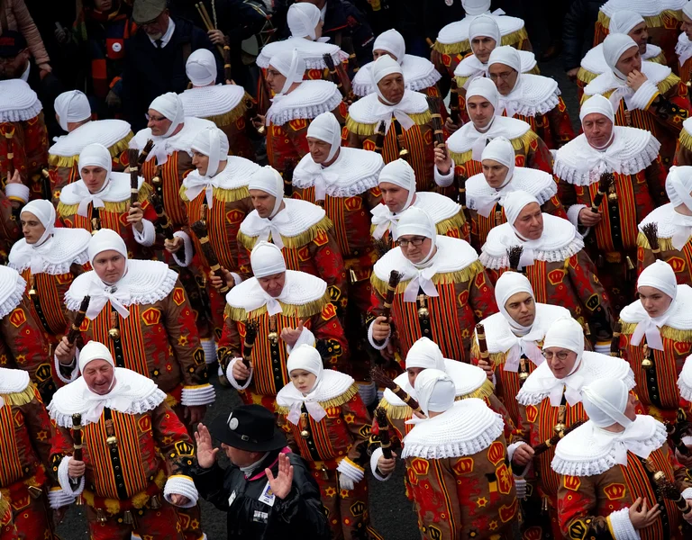 Crowd of people in colorful costumes and white headdresses at a festival parade.