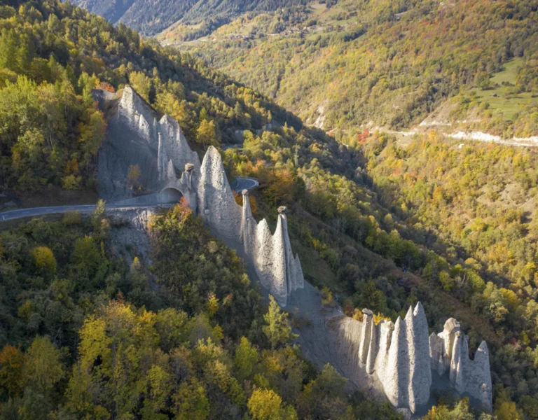 Tall rock spires rise from a forested hillside in a mountainous landscape.