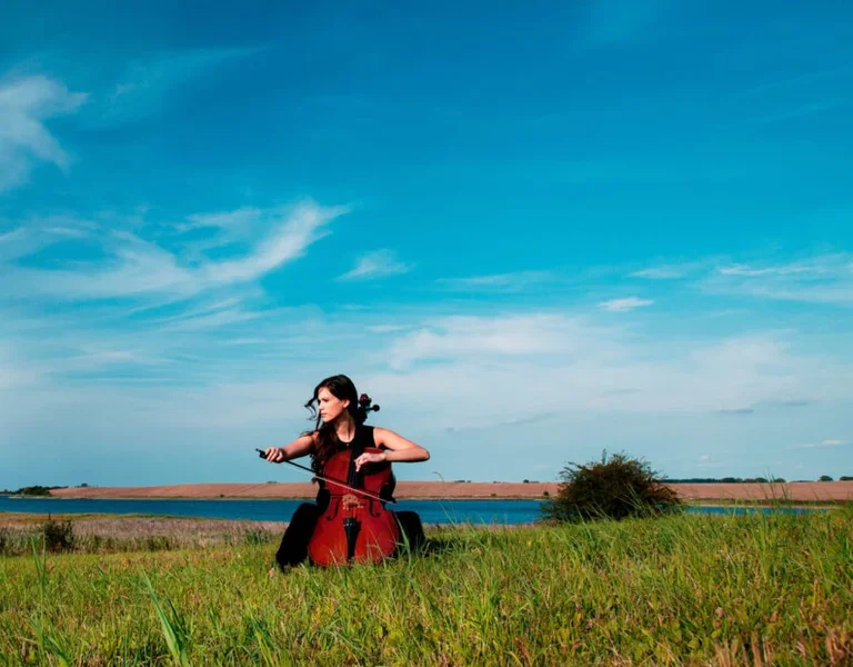 Woman in a red dress running through a grassy field under a bright blue sky.