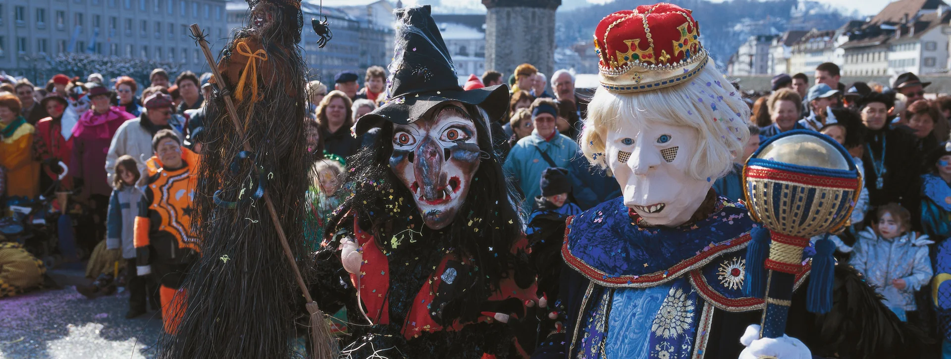People in elaborate Carnival costumes at the Fasnacht event in Lucern with confetti on the ground.