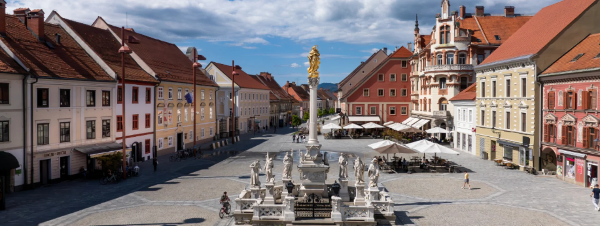 A scenic view of Maribor main square featuring ornate buildings, cobblestone paths, and a prominent fountain surrounded by sculptures.